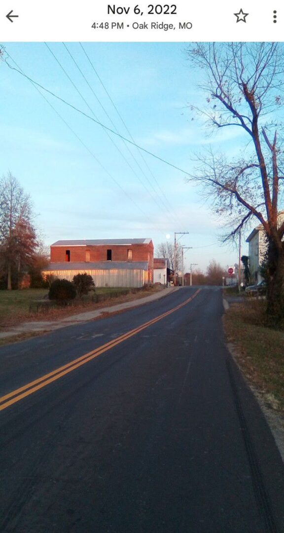 Rural road with trees and buildings, sunset.